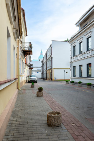 Beautiful narrow old street with historical buildings, flower pots and a church dome under blue sky.