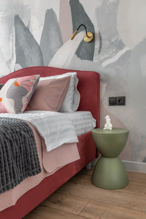 Stylish modern bedroom with pink upholstered bed, abstract wallpaper, wooden floor, and elegant...