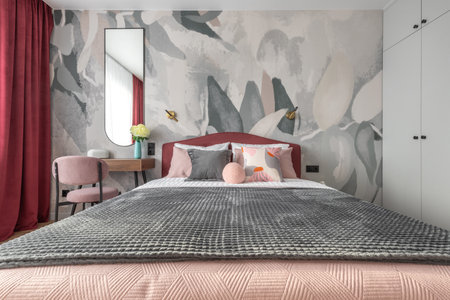 Contemporary bedroom with pink bed, gray blanket, artistic wallpaper, and red curtains creating a cozy elegant atmosphere.の写真素材