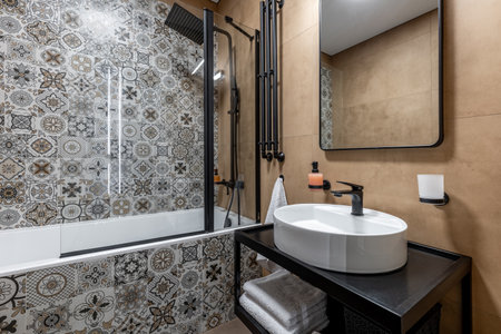 Modern bathroom interior with decorative patterned tiles, stylish lighting, round sink, black...