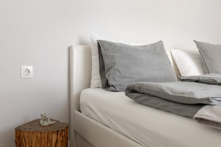 Cozy minimalist bedroom with soft gray bedding, wooden nightstand, and neutral tones creating a calm...