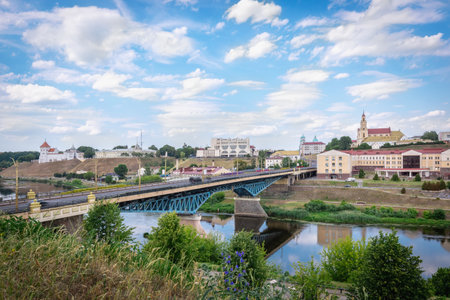 Panoramic view of Grodno city with bridge over the Neman River, historic buildings, and bright summer sky with scattered clouds.の写真素材