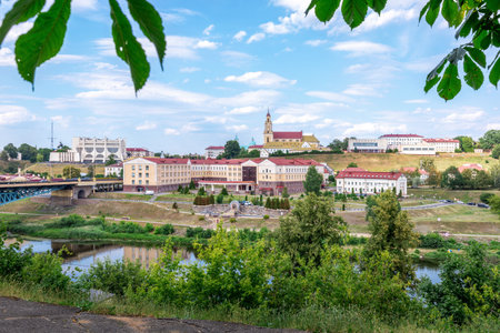 Panoramic scenic view of Grodno city with the Neman River, historic buildings, church, and green trees under a bright summer sky.の写真素材