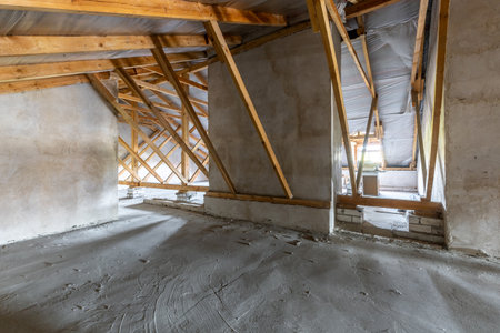 Unfinished attic interior with raw concrete floor, plastered walls, and exposed wooden roof...