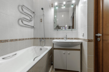 Clean bathroom interior featuring a bathtub, sink cabinet, wall mirror with lights, and tiled walls.