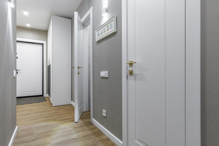 Bright modern apartment hallway with white doors, golden handles, wooden floor, and gray walls...