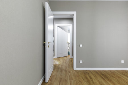 Minimalist interior with white door, golden handle, wooden floor, and gray textured walls in modern...