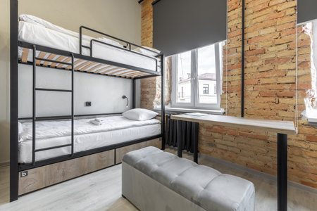 Interior of a modern hostel room featuring a black metal bunk bed with white linens and wood panels....