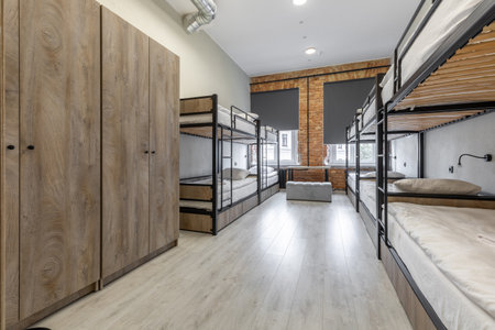 A spacious hostel room featuring large wooden wardrobes and several black metal bunk beds with wood...