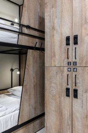 Interior view of a modern hostel dormitory featuring wooden bunk beds with integrated reading lights...
