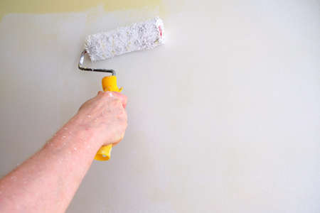 man's hand painting a wall white with a rollerの写真素材