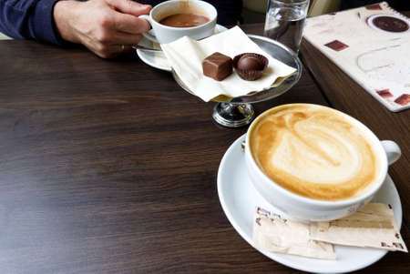 man drinking hot chocolate, cappucino and eating pralines in a cafeの写真素材