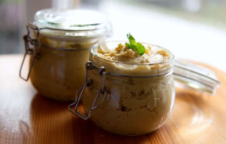 two glass jars of vegan home-made hummus on wooden table