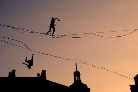 silhouettes of two men at a slackline competition at sunset one walking one fallingの写真素材