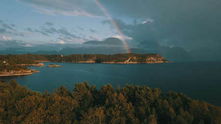 The rainbow on a background of mountains, in the foreground a rock bay of a small town. More og Romsdal, Norway 2019の写真素材