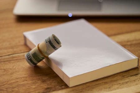 Book with money roll and Laptop on wood background layoutの写真素材