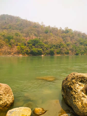 River Ganges flowing from the edge of the forest, stones lying on the banks.の写真素材