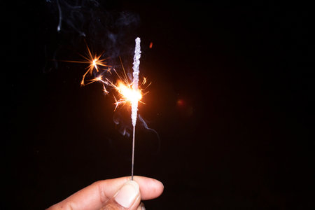 sparkler in hand on black background, closeup of photo