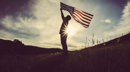 Silhouette of man holding an American flag in the field.の素材