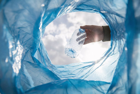 Close-up of human hand holding empty plastic bag against blue skyの素材
