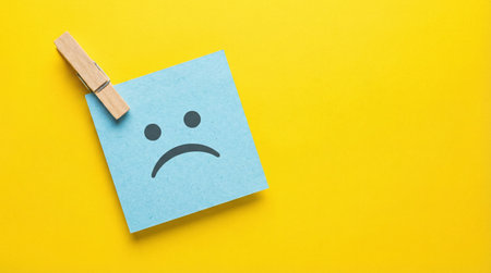 Sad face on note paper with clothespin on yellow background, copy spaceの素材