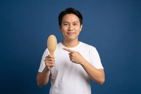 asian young man holding a wooden massage brush on a blue backgroundの素材