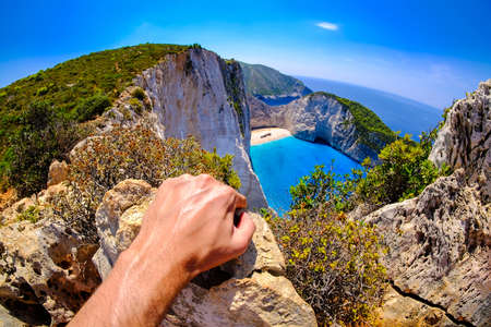 Tourist looking at Navagio Shipwreck panoramic scenic view spot in Zakynthos island Greece. Artistic interpretation. Focus on hand.の写真素材