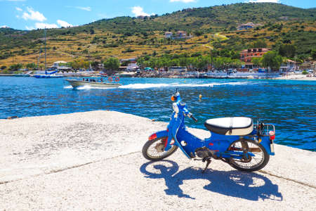 Agios Nikolaos Port Zakynthos island in the summer, with clear blue water, old rusty scooter and hispeed boatの写真素材