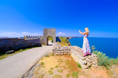 Woman taking pictures at Cape Kaliakra, Bulgaria, Black Sea. Old abandoned fortress by the sea. Important tourist attraction.の写真素材