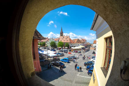 Sibiu, Transylvania, Romania. Daily life in the Small Square (Piata Mica) with the old Catholic Cathedral and the Liars Bridge visible in the back. Important tourist attraction. Artistic interpretation. Window.のeditorial素材