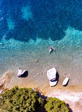 Young woman floating and swimming in beautiful ethereal natural sea, aerial view
