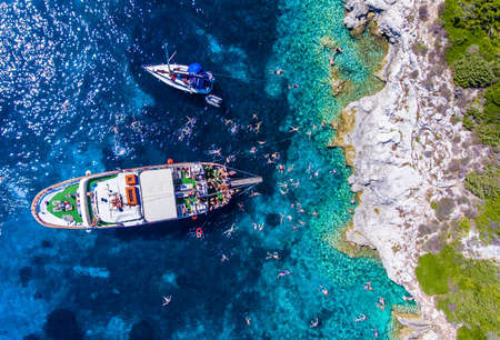 People swimming in the clear blue waters of Antipaxos Island, near Corfu - Kerkyra, Greece. Daily boat trips to the small island from Gaios town, Paxos.のeditorial素材