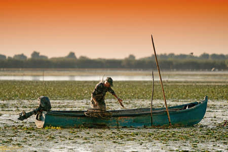 Danube Delta, Romania, August 2017: Traditional Fisherman catching fish at sunrise in Delta Dunarii, Romaniaのeditorial素材
