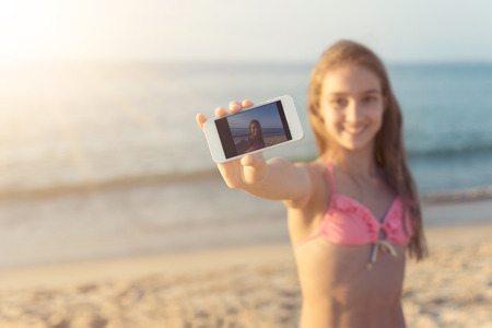 Young woman taking selfie at the sandy beach with the sea and horizon in the background on hot summer day travel and tourism conceptの写真素材