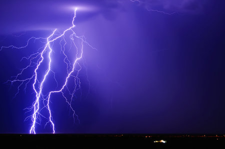 A trio of purple lightning bolts over a remote area of Arizona west of the tiny town of Tonopah during the 2013 Monsoon Season. The lone house in the foreground gives a sense of the isolation. The streaks of light in the distance beneath the lightning are car lights speeding along the I-10 Freeway.の写真素材