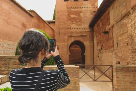 Granada, Spain - 5/6/18: Building of moorish architecture, beautiful orange clay walls and details. Young girl taking a picture on mobile. Alhambra.のeditorial素材