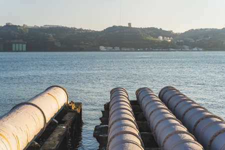 Industrial white pipes near Tejo power station in Lisbon, feeding into the tagus river, Christ King and Bridge in the background, Portugalの写真素材
