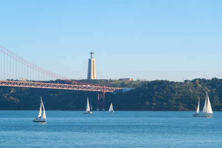 Sailboats with white sails on the Tagus River, 25 of April (25 de abril) Bridge, Christ the king elevator tower in the background, Lisbon, Portugalの写真素材