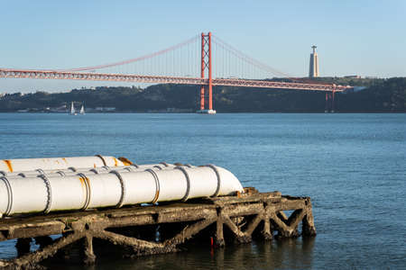 Industrial white pipes near Tejo power station in Lisbon, feeding into the tagus river, Christ King and Bridge in the background, Portugalの写真素材
