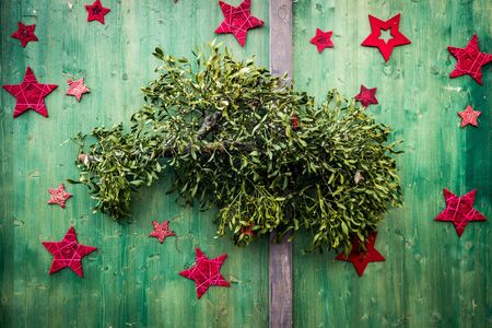Christmas mistletoe plant with red stars around on green wooden background.の写真素材