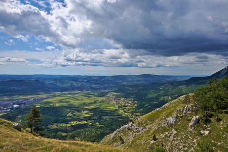 Beautiful view from the mountains towards the valley and the sea in the background. Rainy clouds in the blue sky. Vipava, Slovenia.の写真素材