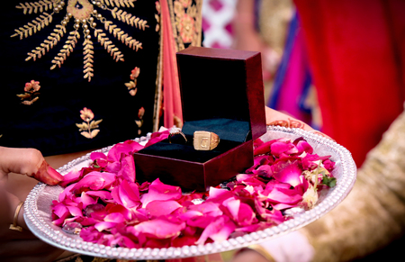 box with a gold wedding ring with a diamond is in the petals of red roses