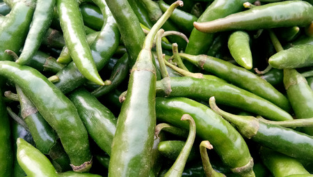 close up view of a pile of green chili pepper in harvest season placed in a market or bazaar for saleの写真素材