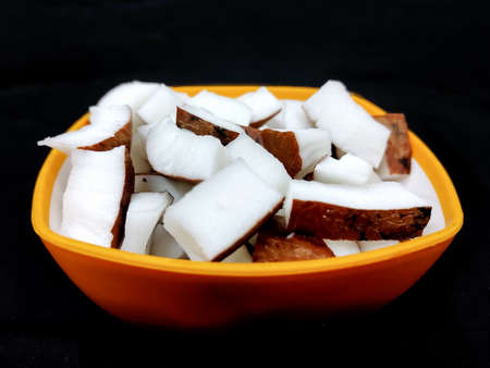 Fresh coconut pieces in a bowl on dark color background with copy space