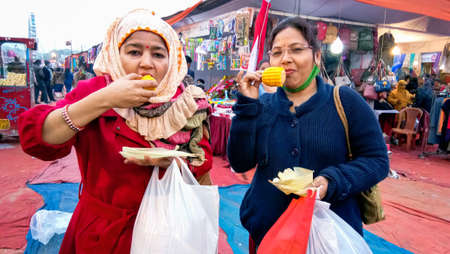 Lucknow, India, January 2021 : Two women eating street food boiled corn (Bhutta) together in outdoor market at day time at lucknowのeditorial素材