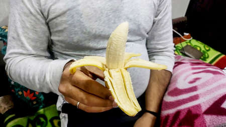 A Young asian man in white t-shirt peeling banana with hand in handの写真素材
