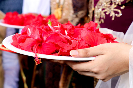 A closeup shot of Indian woman holding a plate with flower petals with henna in her hands in Indian ritualの写真素材