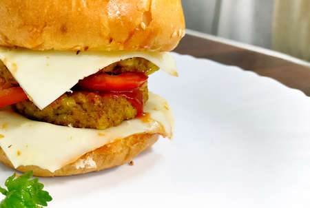 A Close-up of delicious fresh home made burger with aloo tikki, cheese, onion and tomato on a white plate on wooden table backgroundの写真素材