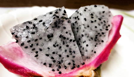 A close-up image of a vibrant dragon fruit (pitaya) split in half, displaying its white flesh dotted with black seedsの写真素材