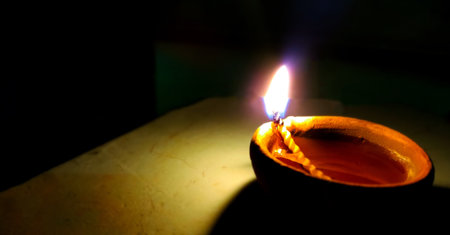 A traditional clay oil lamp (diya) with a burning cotton wick glowing softly in the dark, symbolizing hope, devotion, and the triumph of light over darkness in Hindu culture and festivals like Diwali.の写真素材